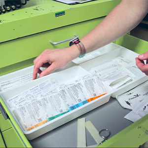 A persons hand organizes medical supplies in a green drawer, sorting packaged items in a white tray.